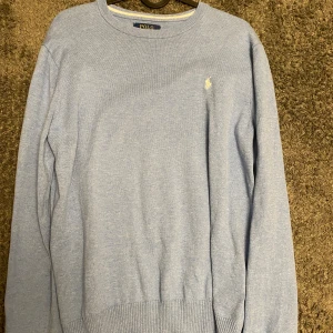 Ljusblå tröja från Polo Ralph Lauren - Snygg ljusblå tröja från Polo Ralph Lauren i mjuk pima bomull. Klassisk rund halsringning, ribbade muddar och diskret broderad logga på bröstet. Perfekt för dig som gillar stilren och enkel design. Bara att höra av sig vid minsta funderingar🙌🌟