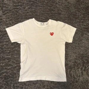 Vit Comme des Garçons Play t-shirt - Vit t-shirt från Comme des Garçons Play med det ikoniska röda hjärtat med ögon broderat på bröstet. Klassisk passform, rund hals och korta ärmar. Tillverkad i mjuk bomull för en skön känsla. Storlek M men sitter som en S då dem är väldigt små i storleken.