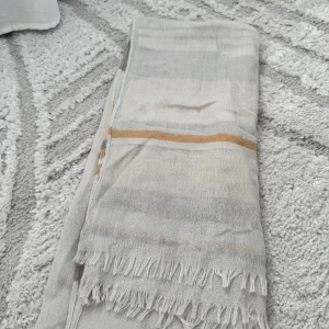 Randig halsduk från Pieces i beige toner - Snygg och tunn halsduk från Pieces med randigt mönster i beige, grått, vitt och ljusbrunt. Halsduken har fransar i kanterna och är perfekt att slänga över axlarna för en chill look. Lätt och luftig, passar bra till både jacka och tröja.