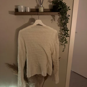 Vit långärmad tröja från Gina Tricot - Säljer en vit långärmad tröja från Gina Tricot i storlek M. Tröjan har ett vågigt, strukturerat tyg som ger en cool och unik look. Perfekt att styla med jeans eller kjol för en fräsch vibe.