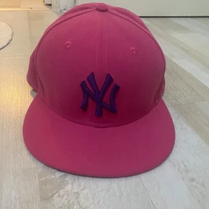 Rosa New Era Yankees keps 59FIFTY - Säljer en rosa New Era 59FIFTY keps med New York Yankees-logga i lila framtill. Kepsen har klassisk rak skärm och broderade detaljer, samt MLB-logga bak. Tillverkad i bomull och passar dig som vill sticka ut med färg.