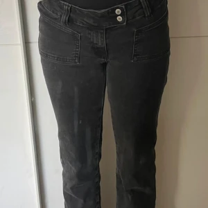 Svarta bootcut jeans från 157 - Snygga svarta jeans från 157 med bootcut passform och låg midja. Jeansen har två framfickor, dubbla knappar i midjan och klassisk femficksdesign. Materialet är mjukt och stretchigt jeans, perfekt för en chill och trendig look. Storlek S / Short 