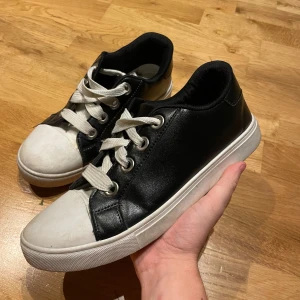 Svarta och vita sneakers med snörning - Snygga sneakers i svart och vitt med klassisk design. Skorna har vita snören, rund tå och platt sula. Ovandelen är i svart material med vita detaljer på tå och sula. Perfekta för en stilren och avslappnad look. Köpte dem i Italien så kommer inte ihåg märke det stog i sulan förr men har tyvärr försvunnit.