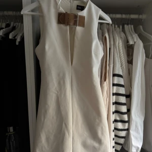 Vit ärmlös kortklänning från Zara - Supersnygg vit ärmlös kortklänning från Zara med markerad midja och coolt brunt bältedetalj framtill. 