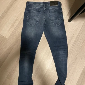 Mörkblå Replay Jeans Anbass - Snygga mörkblå Replay Anbass jeans med klassisk femficksdesign och diskret slitning på låren. Jeansen har en slim passform och är tillverkade i stretchigt jeansmaterial för extra komfort. Perfekta för dig som gillar en modern och stilren look.
