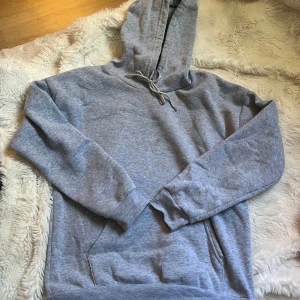 Grå hoodie med magficka och snörning - En klassisk grå hoodie med huva och snörning, perfekt för chill dagar. Tröjan har en stor magficka och ribbade muddar vid ärmslut och nederkant. Tillverkad i mjuk bomullsblandning för extra komfort.