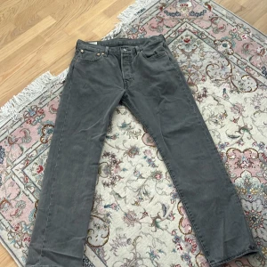Grå Levi's 501 jeans W32 L32  - Säljer ett par grå Levi's 501 jeans i relaxed straight modell. Jeansen har fyra fickor, knappgylf och den ikoniska läderpatchen bak i midjan. Tillverkade i slitstarkt denim med snygg tvättad grå färg. Perfekta för dig som gillar tidlös stil. Använd ändast 1 gång!