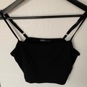 Svart croppad linnetopp från SHEIN - En svart croppad linnetopp från SHEIN med smala, justerbara axelband. Toppen har en enkel och stilren design med rak halsringning och är tillverkad i mjuk bomullsmix. Perfekt att matcha med jeans eller kjol för en trendig look.