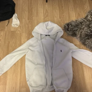 Vit hoodie från Polo Ralph Lauren S - Vit hoodie från Polo Ralph Lauren i storlek S. Tröjan har huva, två fickor fram och klassisk Polo-logga broderad på bröstet. Tillverkad i mjuk bomull med fleece på insidan. Dragkedjan är sönder.