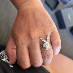 Playboy silverring med glittrande stenar - Snygg ring i silverfärg med ikoniska Playboy-kaninen täckt av glittrande stenar. Ringen har en cool och lekfull design som sticker ut och passar perfekt för dig som vill ha något unikt och trendigt.