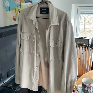 Overshirt Mads Nørgaard - Snygg beige overshirt från Mads Nørgaard med klassisk krage och två stora bröstfickor med knappar. Skjortan har långa ärmar och är gjord i mjuk bomull. 