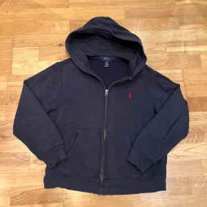 Polo Ralph Lauren hoodie - Snygg mörkblå hoodie från Polo Ralph Lauren med röd logga på bröstet. Tröjan är använd men fortfarande i bra skick utan några synliga defekter. Priset är prutbart.