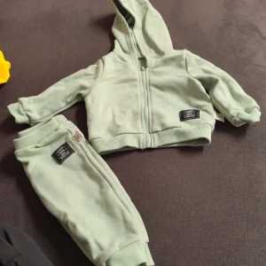 Mintgrön hoodie från SHEIN baby - Supermjuk mintgrön hoodie från SHEIN för baby, med dragkedja framtill och huva. Tröjan har långa ärmar och ribbade muddar. Perfekt för chill dagar och matchas snyggt med de medföljande byxorna. Stilren patch-detalj på både tröja och byxa.