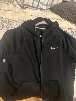 Svart Nike fleece  - Svart vindjacka från Nike med huva och vit logga på bröstet. Jackan har dragkedja framtill, praktiska fickor och en sportig look. Håller värme bra och är perfekt för vintern. Köpt ifrån Zalando, priset kan diskuteras. Säljer den pga av jag har gott när i vikt jätte mycket den passar inte mig längre.