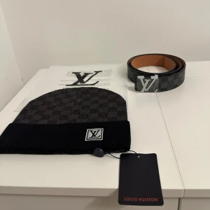 Svart och grå L.V mössa/Bälte - Snygg mössa L.V i svart och mörkgrått med klassiskt rutigt mönster och L.V-logga framtill. Mössan har uppvikt kant och är tillverkad i mjukt stickat material som känns lyxigt och bekvämt. Perfekt accessoar för att lyfta din stil.