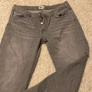 Grå jeans straight fit 157 - Grå jeans från 157 med klassisk femficksdesign och raka ben. Jeansen har en enkel knappgylf och diskreta slitningar vid benslutet för en avslappnad look. Perfekta för dig som gillar en basic och stilren vibe.