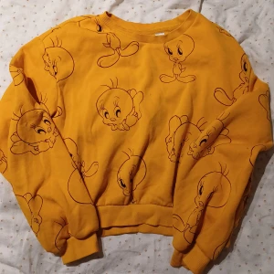 Looney Tunes Gul Fågel Tweety Pip Tröja Sweatshirt H&M Divided - En Supergullig Mörkgul Gul Sweatshirt från H&M x Looney Tunes. Storlek M. Lite croppad i längden. (Övre mittenkant - Nedre mittenkant): Ca 42 cm. Gott skick men har en pytteliten fläck mitt på tröjan, syns på bilderna. Försvinner troligtvis i tvätt. 🌷