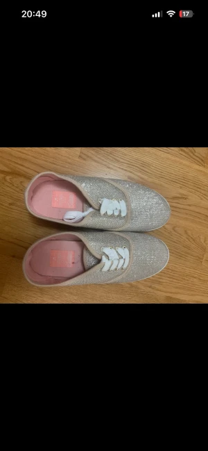 Glittriga sneakers med vit sula - Säljer ett par snygga sneakers från Kate Spade med glittrigt silverfärgat tyg och vita snören. Insidan är ljusrosa och sulan är helt vit och platt. Perfekta för dig som vill sticka ut med lite extra glitter i vardagen. Aldrig använda storlek 39 