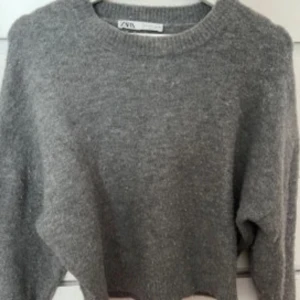 Grå stickad tröja från Zara - Mysig grå stickad tröja från Zara med rund hals och ribbade muddar vid ärmslut och nederkant. Tröjan har en klassisk, loose passform och är perfekt för att hålla värmen under kyliga dagar. Enkel och stilren design som funkar till allt. Första bilden är lånad❤️lite nopprig men super skick annars