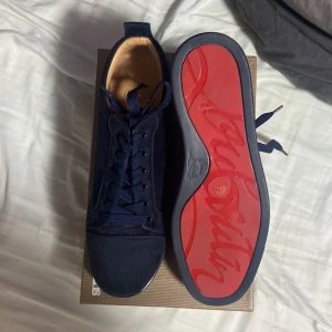 Mörkblå loubs👌 - Säljer ett par mörkblå sneakers från Christian Louboutin med klassisk röd sula och rund tå. Skorna har snörning och är tillverkade i mjuk mocka med beige innersida. Snygg och stilren design som sticker ut med den ikoniska röda undersidan.