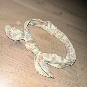 Blommigt diadem från Newbie pannband hårband  - Sött diadem från Newbie i ljusbeige bomullstyg med blommigt mönster i rosa, blått och grönt. Diademet har en knut framtill som ger en extra gullig touch. Perfekt för att piffa upp din look med lite vintage-vibe.Ett sött hårband från Newbie med ett blommigt mönster och knutdetalj.