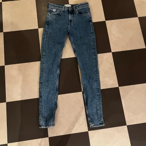 Slim tapered jeans från Calvin Klein - Snygga blå jeans från Calvin Klein med slim tapered passform. Klassisk femficksdesign, med CK-logga på bakfickan och vit etikett i midjan. Jeansen har smal siluett och är tillverkade i mjukt denimtyg med orangea sömmar.
