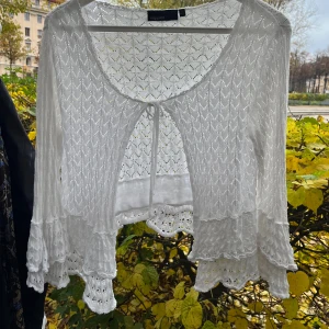 Vit bolerotopp med volang från KappAhl - Supersöt vit bolerotopp från KappAhl med virkade detaljer och volangkant. Toppen är croppad, har knyt framtill och långa ärmar med extra volang. 