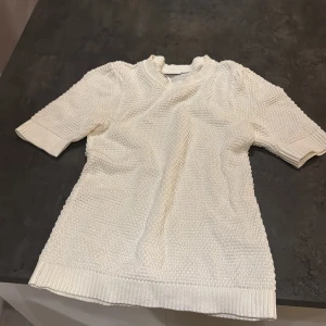 Vit stickad tröja med kort ärm - Säljer en vit stickad tröja med korta ärmar och ribbade muddar vid hals, ärmslut och nederkant. Tröjan har en snygg strukturstickning som ger en cool och trendig känsla. Perfekt för dig som gillar en stilren look.💞💞