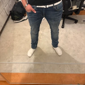 Levi's 511 blå jeans med vit bälte - Säljer ett par Levi's 511 jeans i klassisk blå tvätt med snygga slitningar och vit bälte. Modellen är slim fit med normal midja och raka ben. Jeansen har fem fickor och är tillverkade i mjukt jeanstyg som sitter skönt hela dagen.