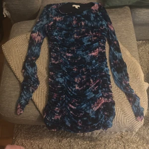 Blå och rosa mönstrad klänning H&M - Säljer en cool kort klänning från H&M i storlek L , jag tycker den är mer åt M med blått och rosa abstrakt mönster. Klänningen har lång ärm, rynkade detaljer framtill och är figurnära. Materialet känns mjukt och stretchigt, perfekt för dig som gillar att sticka ut med färg och form.