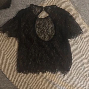 Svart spetsblus från Bershka XS - Säljer en svart, transparent spetsblus från Bershka i storlek XS. Blusen har korta ärmar, rund halsringning med knappdetalj i nacken och är helt i spets med fina kanter. Perfekt för att skapa en edgy och trendig look.