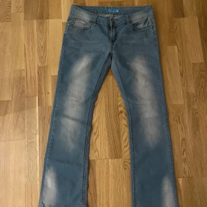 Bootcut jeans från D-xire, ljusblå - Snygga ljusblå bootcut jeans från D-xire med klassisk femficksdesign och coola slitningar framtill och baktill. Materialet är 95% bomull och 5% polyester, vilket gör dem både mjuka och slitstarka. Bakfickorna har en extra dragkedja för en unik touch.