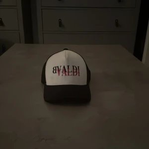 Svartvit keps från BVALDI - Snygg svartvit keps från BVALDI med tydlig logga framtill i svart och rosa. Framsidan är vit med tryck, medan baksidan är svart mesh för extra ventilation. Justerbar passform och cool streetstil, perfekt för dig som vill sticka ut.