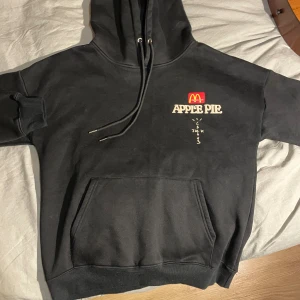 Svart Cactus Jack x McDonald's hoodie M - Svart hoodie från Cactus Jack x McDonald's med tryck 'APPLE PIE' och McDonald's-logga fram, samt 'ALWAYS HAD A THING FOR SWEETS' och Cactus Jack-tryck bak. Stor känguruficka, snörning i huvan och mjukt material i bomull och polyester. Perfekt för dig som gillar limited edition streetwear.