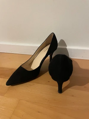 Svarta Rizzo-pumps med spetsig tå - Svarta pumps från Rizzo med spetsig tå och smal klack. Skorna är tillverkade i mocka och har en elegant, klassisk design. Klacken är medelhög.