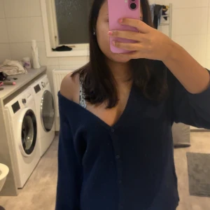 Mörkblå kofta med v-ringning - Säljer en mörkblå kofta med djup v-ringning och knappar framtill. Koftan har en loose passform och långa ärmar, perfekt för att slänga över en topp. Materialet är mjukt och stickat, vilket gör den extra skön att bära.