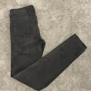 Replay svarta slim jeans 30/34 - Svarta jeans från Replay i slim fit-modell med klassiska fem fickor och snygga detaljer på bakfickorna. Jeansen har en smal passform och är tillverkade i stretchigt bomullsmaterial för extra komfort. Perfekt för dig som gillar stilrena och moderna jeans.