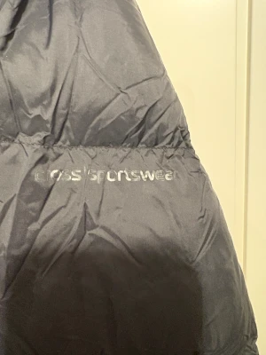 Svart pufferjacka från Cross Sportswear - Svart pufferjacka från Cross Sportswear med hög krage och dragkedja framtill. Jackan har ett stilrent, quiltat mönster och är tillverkad i syntetmaterial. Perfekt för kalla dagar med sin tjocka och fluffiga design.