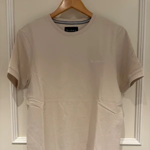 Bondelid T-shirt - Snygg beige t-shirt från Bondelid med diskret logga broderad på bröstet. Klassisk rund hals och korta ärmar. Mjuk och skön bomullskvalitet som känns fräsch mot huden. Perfekt basic-plagg med stilren look. Tröjan har storlek M och helt ny och aldrig använd