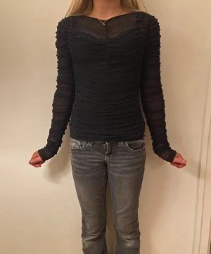 Svart glittrig mesh-top från H&M Divided - Säljer en svart långärmad mesh-top från H&M Divided i storlek XXS. Toppen har glittriga detaljer och är figurnära med rynkade sömmar längs hela plagget. Perfekt för dig som gillar en trendig och snygg look med lite extra glitter. Parfekt till nyår eller jul. 
