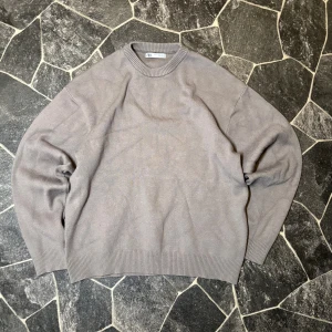 Zara stickad tröja - En enkel och stilren grå stickad tröja från Zara med rund hals och ribbade muddar vid hals, ärmslut och nederkant. Perfekt för lager-på-lager och passar till jeans eller chinos. Klassisk modell med lång ärm och mjukt material.