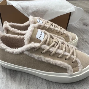 Beige sneakers från Inuikii - Säljer ett par beige sneakers från Inuikii. Skorna har snörning, platt vit sula och ovandel i mocka. Perfekta för dig som vill ha både stil och värme under kyliga dagar.