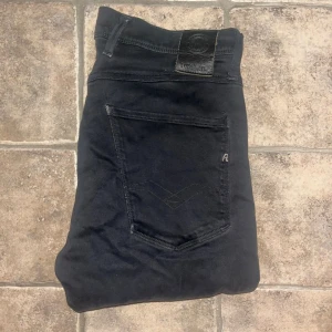 Replay Anbass jeans - Snygga svarta Replay Anbass jeans med smal passform och klassisk femficksdesign. Byxorna har diskreta svarta sömmar, dragkedja och knappstängning. Materialet är mjukt och stretchigt för extra komfort. Midja 39cm, längd 101cm. JAG SKICKAR EJ FLER BILDER NÄR JAG BÄR JEANSEN! för storleksguide hänvisar jag till måtten och för bättre inblick i passformen rekommenderar jag att googla på modellnamnet. Jeansen kan vara uppsydda utan att jag noterat det så kolla måtten noggrant :) s4