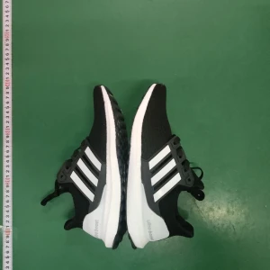 Adidas Ultraboost svarta sneakers - Svarta Adidas Ultraboost sneakers med klassiska vita ränder på sidan och vit sula. Skorna har snörning och en rund tå, tillverkade i syntet och textil för maximal komfort och stil. Perfekta för dig som gillar sportig look och vill ha riktigt sköna skor.