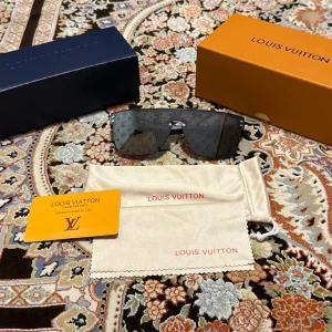 Svarta monogram-solglasögon Louis Vuitton - Snygga svarta solglasögon från Louis Vuitton med spegelglas och ikoniskt LV-monogram över hela linsen. Sköldformad modell med breda glas och minimalistisk båge. Kommer med originalbox, fodral och putsduk.