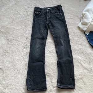 Svarta low waist bootcut jeans - Snygga svarta jeans med bootcut passform och vita kontrastsömmar. Klassisk femficksmodell med knappar på bakfickorna och lätt slitning framtill. Jeansen har normal midja och är tillverkade i mjukt denimtyg som sitter skönt hela dagen.