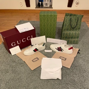 Gucci Ace skor - Säljer dessa Gucci ace skor i storlek 44 de är helt nya och aldrig använda .Gucci Ace sneakers i vitt skinn med klassiska gröna och röda sidoremsor. Ena skon har broderad röd orm och detaljer i rött och grönt på hälen. Lyxig design med ikoniska Gucci-detaljer, levereras med originalkartong och dustbags. Priset kan diskuteras vid snabb affär.
