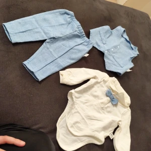 Babykostym med blå väst och byxa - Supersöt babykostym från SHEIN med ljusblå väst och matchande byxor i mjukt tyg. Till setet hör en vit långärmad body med krage och blå fluga. Perfekt för speciella tillfällen när du vill att din lilla ska vara extra stilig.