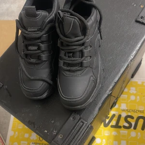 Chunky svarta sneakers med platåsula - Säljer ett par chunky svarta sneakers med kraftig platåsula och snörning. Skorna har en sportig vibe med robust design och detaljerade sömmar. Tillverkade i syntetmaterial och passar perfekt för dig som gillar streetstyle och vill sticka ut.