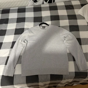 Ljusgrå stickad tröja från Massimo dutti - Snygg ljusgrå stickad tröja från Massimo dutti med rund hals och ribbade muddar vid ärmslut och nederkant. Perfekt för dig som gillar enkel och stilren design. Tröjan har lång ärm och är gjord i mjuk bomull som känns skön mot huden.